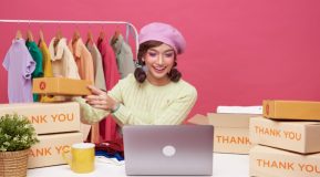 Girl in pink beret in front of Apple laptop with clothes hanging on a rail behind her