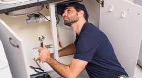 A male plumber kneeling down looking under a kitchen sink unit