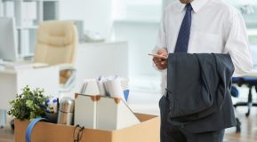 Unrecognizable man standing in office and using smartphone, with personal belongings in box