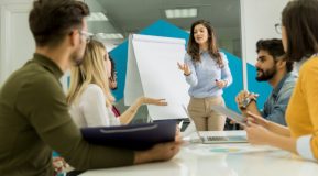 Young business woman standing in front of a flip chart presenting training to a group of employees